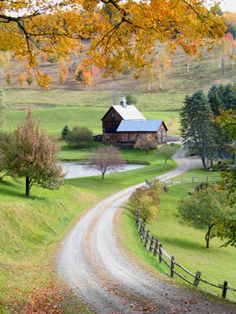 a country road with a barn on the side and trees in the foreground, surrounded by fall foliage