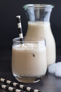 two glasses filled with milk and one has a straw sticking out of the top in front of it