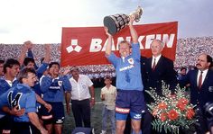 an older man holding up a trophy in front of a group of men on a field