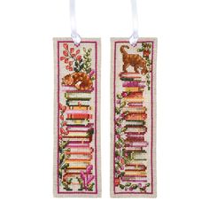 two cross stitch bookmarks with cats and bookshelves hanging from the front, one has