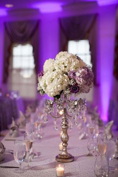 a centerpiece with flowers and candles is displayed on a round table in front of purple lighting