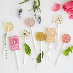 several lollipops are arranged on a white surface with pink flowers and greenery