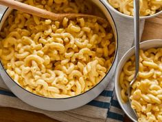 macaroni and cheese is being cooked in two pans with wooden spoons