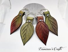 three leather leaf keychains are hanging from a metal hook on a white background