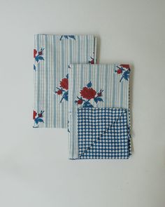 two blue and white napkins with red flowers on them sitting next to each other