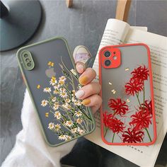 a woman is holding an iphone case with flowers on it and a book next to her