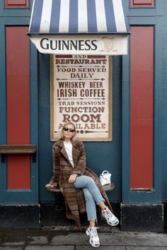 a woman is sitting on a bench in front of a guinness sign and wearing sunglasses