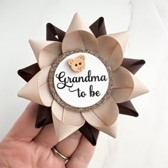 a hand holding a brooch with the words grandma to be on it and a teddy bear