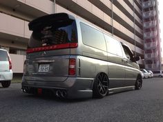 the rear end of a silver van parked in front of a tall building next to another car