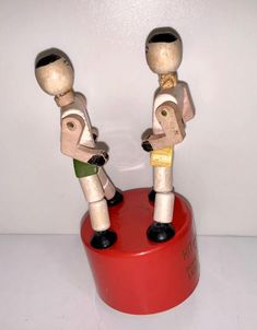 two wooden figurines standing on top of a red container