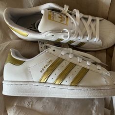 Elevate Your Sneaker Game With These Adidas Superstar Shoes In Size 7 For Women. The Gold Stripes On This Athletic Footwear Add A Touch Of Glam To Your Casual Look. These Sneakers Feature A Classic Design That Never Goes Out Of Style, Making Them A Must-Have In Your Shoe Collection. The Adidas Gold Product Line Ensures You're Getting Quality And Durability With Each Step You Take. Perfect For Any Casual Occasion, These Striped Sneakers Will Keep You Stylish And Comfortable All Day Long. Adidas Gold, Addidas Shoes Super Star, Black And Gold Adidas, Adidas Shoes Women Superstar, Adidas Superstar Gold, Sneakers Adidas Superstar, Adidas Superstar Women, Gold Adidas, Adidas Shoes Superstar