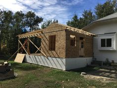 a house being built in front of a white house with wood framing on the roof