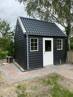 a small gray shed with a white door and windows