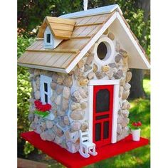 a bird house made out of rocks with a red door and windows on the roof