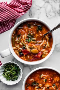 two bowls filled with pasta and spinach soup on top of a white marble counter