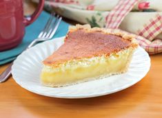 a piece of pie on a white plate with a fork and cup in the background