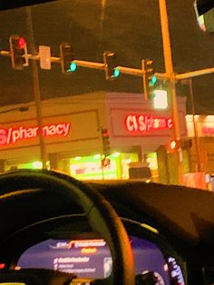 a car driving down a street next to a traffic light and storefronts at night