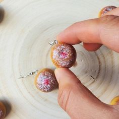 a person is holding three small pastries on top of a wooden plate with other pastries in the background