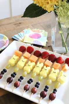 an assortment of fruit and cheese on skewers with flowers in vase behind them