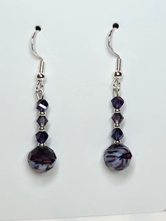 two pairs of earrings with purple beads hanging from the hooks on a white table top