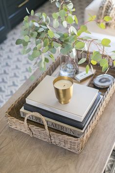 a wicker tray topped with books and a candle on top of a coffee table