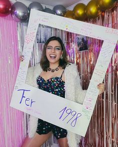 a woman is holding up a sign in front of balloons and streamers as she poses for the camera