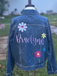 Custom Embroidered Denim Name Jacket with flowers Flowers will be in fun different colors, similar to pictured. If you want specific flower colors, let me know in the notes.  These are Carter's dark denim jackets.  100% Cotton  2T 3T 4T 5T 6, 6X Drop down says 6x but the size is 6, 6x 7 8 10 12 Please refer to their size chart for measuremts before ordering, but they run pretty true to size. Lots more thread color options, so if looking for something specific, let me know! Select thread color for NAME:  *Pictured in sweet lavender. Bubble Gum Cotton Candy Christmas Green Christmas Red Dusty Mauve Gold Guacamole Summer Yellow Sweet Lavender Tukan Blue White CUSTOMIZATION  Please leave the name of the child or the word you want stitched on the back, on the personalization area provided. Plea Spring Denim Jacket With Custom Embroidery And Long Sleeves, Cute Long Sleeve Denim Jacket For Spring, Fun Cotton Outerwear For Spring, Spring Cute Denim Jacket With Pockets, Fun Pink Spring Outerwear, Fun Spring Denim Jacket, Casual Cotton Outerwear With Floral Applique, Cute Fitted Embroidered Outerwear, Spring Blue Denim Jacket With Custom Embroidery