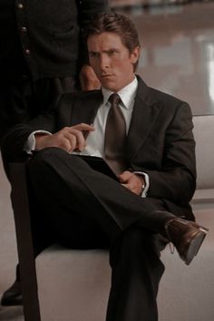 a man in a suit and tie sitting on a white chair with another man standing behind him