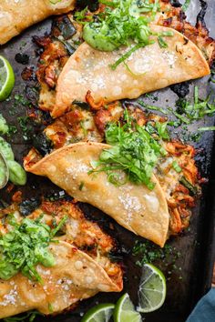 some tacos are sitting on a tray with lime wedges and cilantro