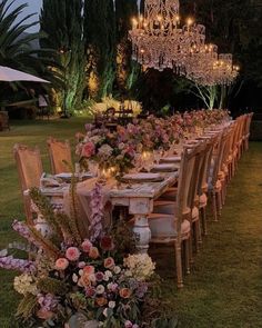 an outdoor dining table set up with chandelier and flowers in the center, surrounded by greenery