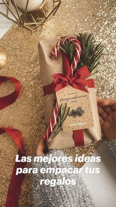 a person holding a wrapped present on top of a table next to a christmas tree