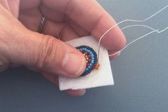 a hand holding a small beaded ring on top of a piece of white cloth