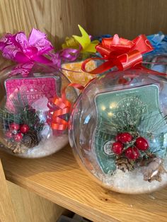 two snow globes sitting on top of a wooden shelf filled with ornaments and bows