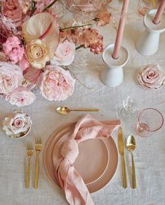 the table is set with pink flowers and gold utensils, napkins, and plates