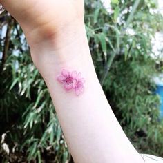 a small pink flower tattoo on the wrist