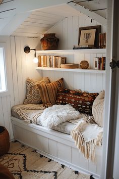 a window seat with pillows and blankets on it in a room that has white walls