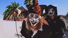 two people dressed up as clowns with palm trees in the background