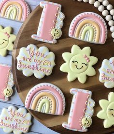 decorated cookies on a wooden platter with rainbows, clouds, and letters that say you are my sunshine