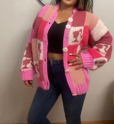 a woman standing in front of a wall wearing a pink and white cardigan