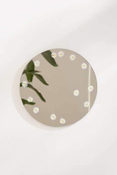 a round mirror with white daisies on the bottom and green leaves in the middle