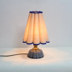 a lamp that is sitting on top of a white table cloth covered surface with a blue trim around the base