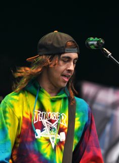 a man with long hair wearing a tie - dyed hoodie and holding a guitar