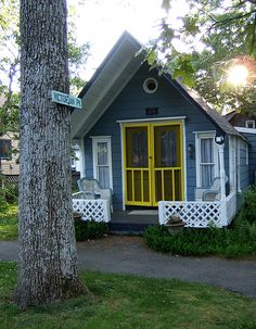 a small blue house with yellow doors and porches next to a tree in front of it