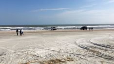 people are walking on the beach near cars