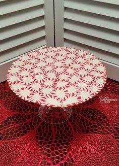 a red and white doily covered cake plate sitting on top of a table next to shutters