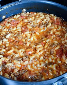 a close up view of macaroni and cheese in a pan with meat on top