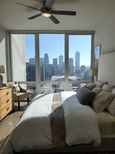 a bedroom with a large bed and a ceiling fan in front of a window overlooking the city