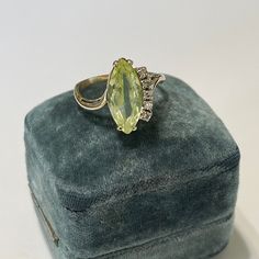 an oval shaped green stone ring sitting on top of a velvet box with diamond accents