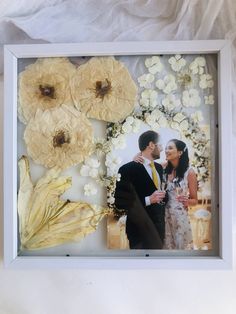 a couple standing next to each other in front of flowers and leaves on the wall