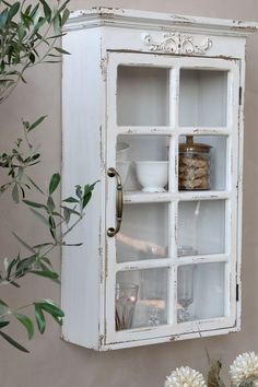 an old white cabinet with glass doors on the side and flowers in vases next to it